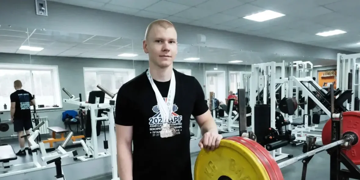 Иван Ежов с медалями рядом со штангой в тренажёрном зале